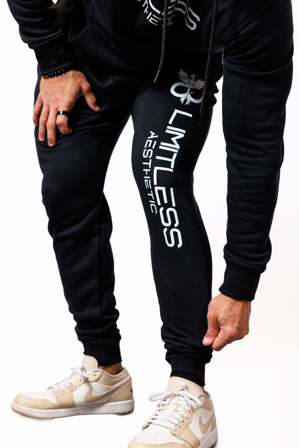 Close-up view of black jogger sweatpants with white text graphics and cream-colored Nike sneakers on white background.