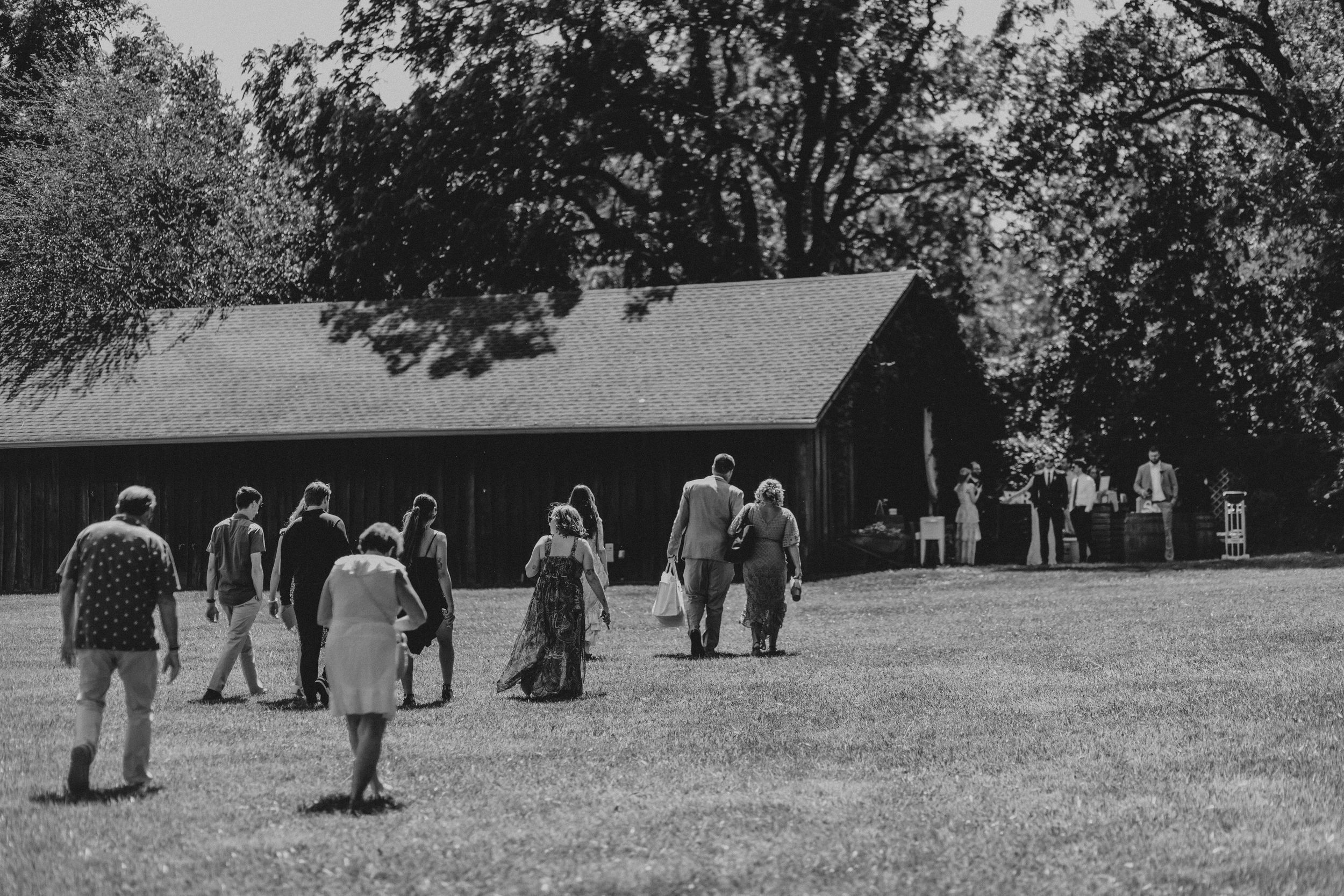 A group of people walking towards a rustic building in a wooded area.