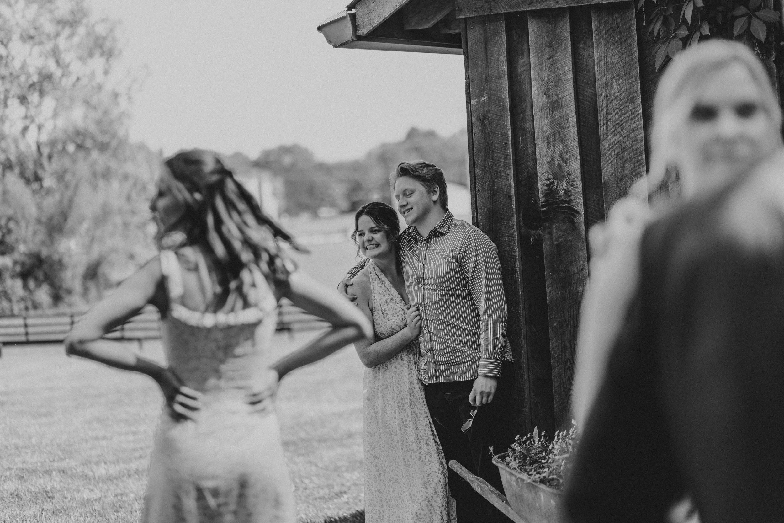 A black and white photo of a wedding scene with people gathered outside a rustic wooden structure.