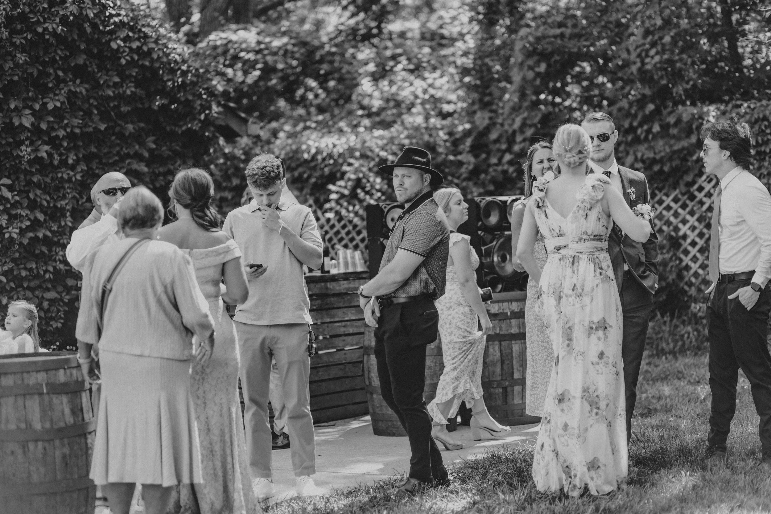 A black and white photo shows a group of people gathered outdoors for a social event in a garden setting.