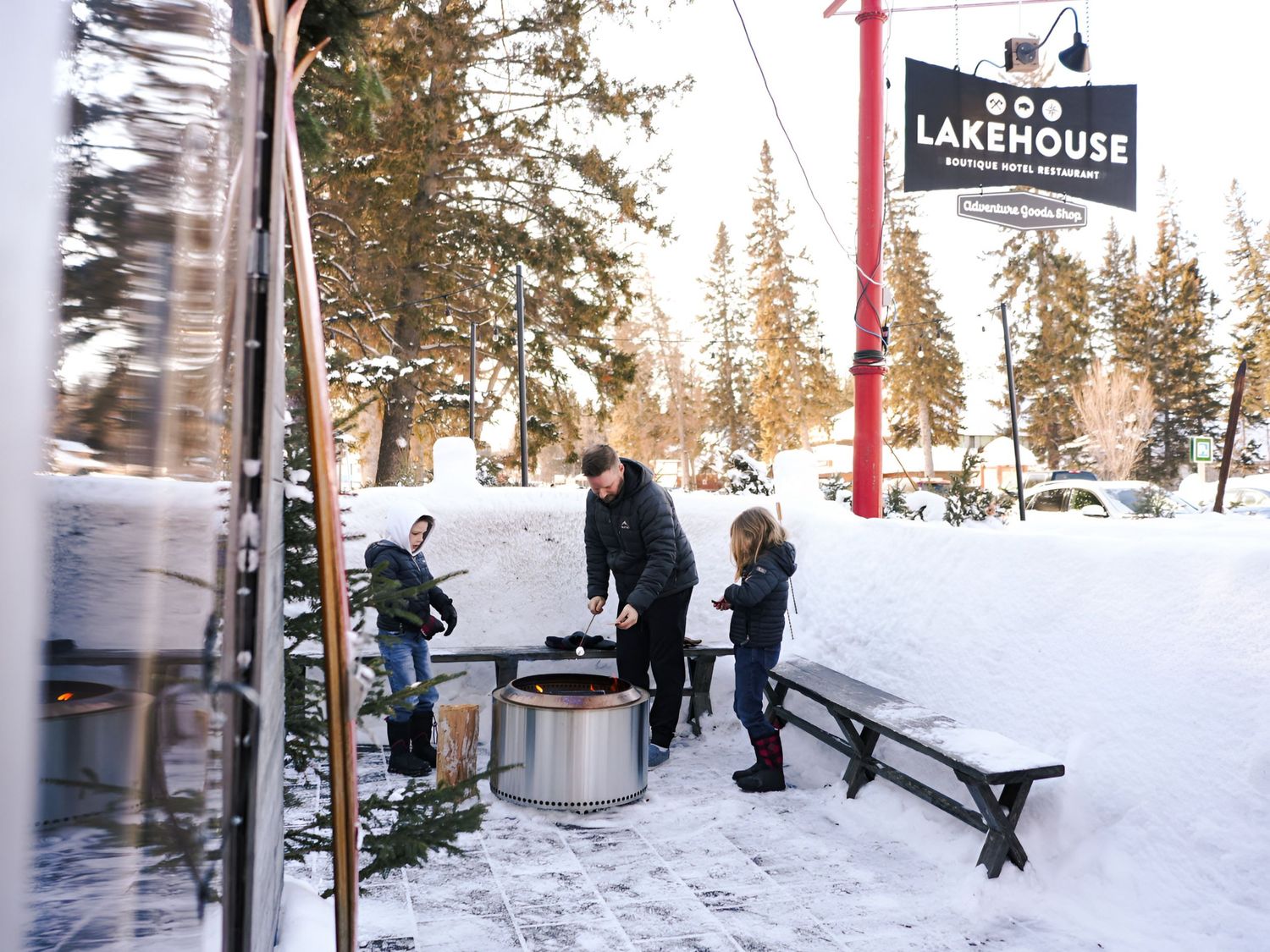 People enjoying winter activities at a snowy mountain resort with ski lifts and lodge buildings visible in the background.