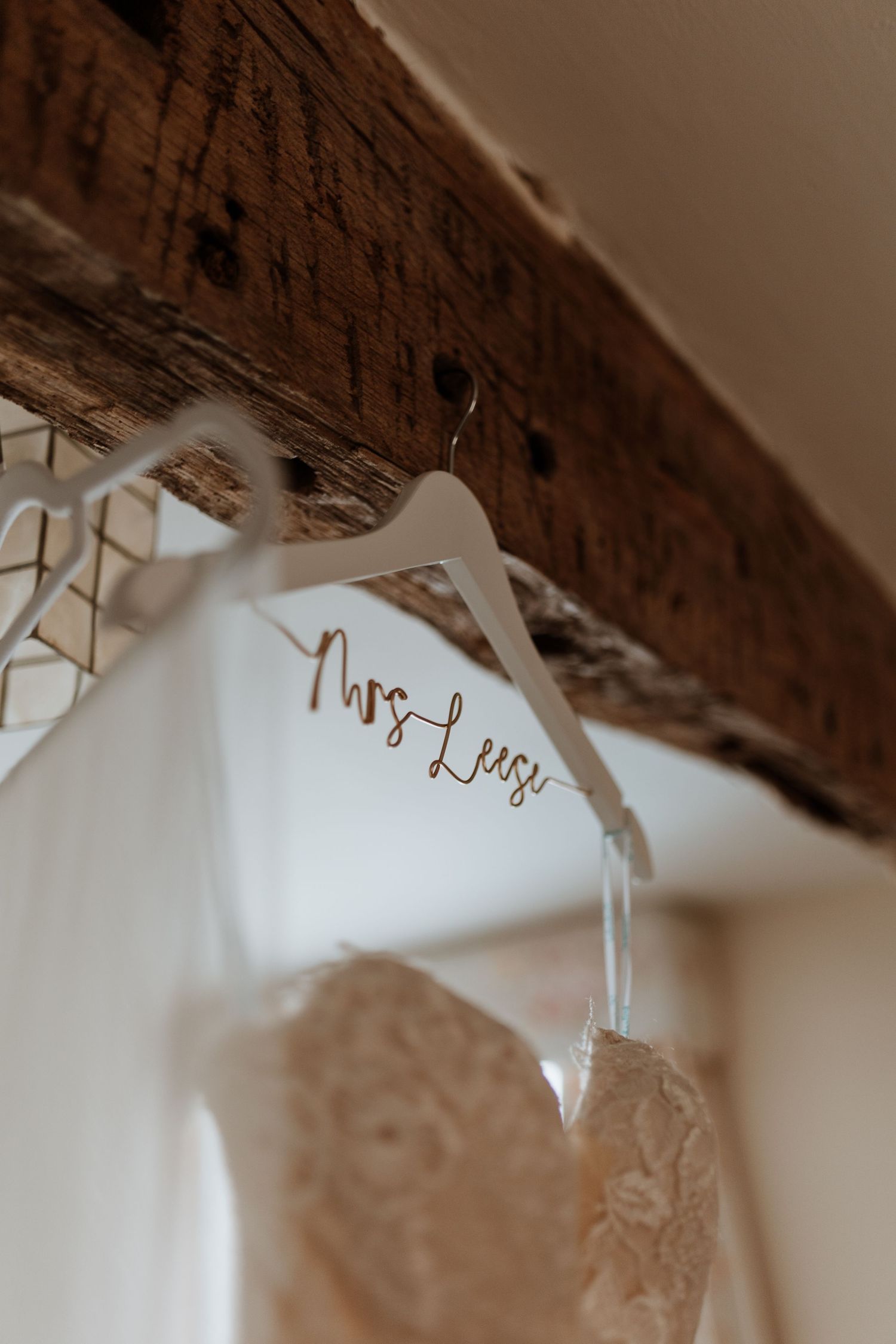 Wedding dresses hanging on personalised white hangers with 'Mrs' text under rustic wooden beams.