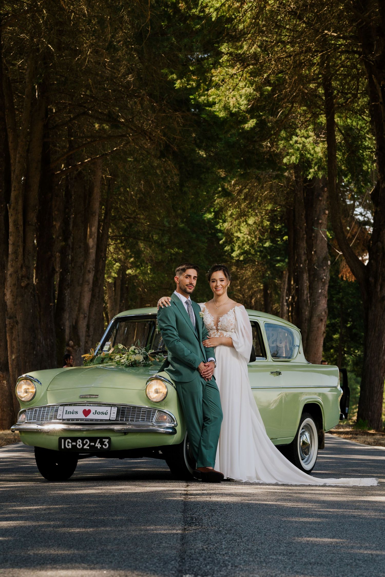 Couple poses with vintage mint green car on tree-lined road.