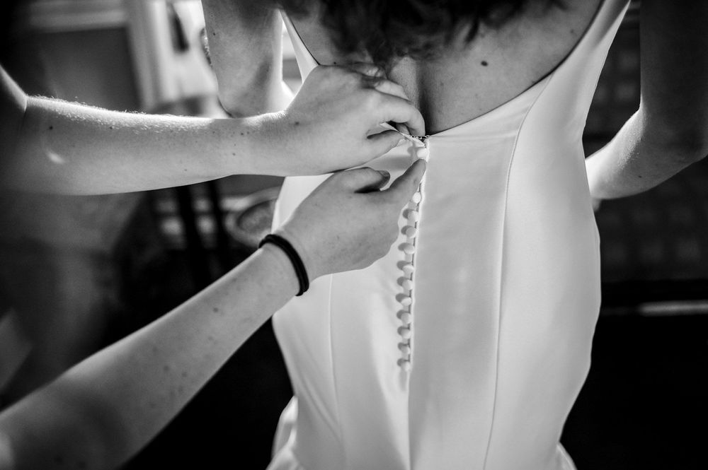 A close-up view of someone fastening the back of a white wedding dress.