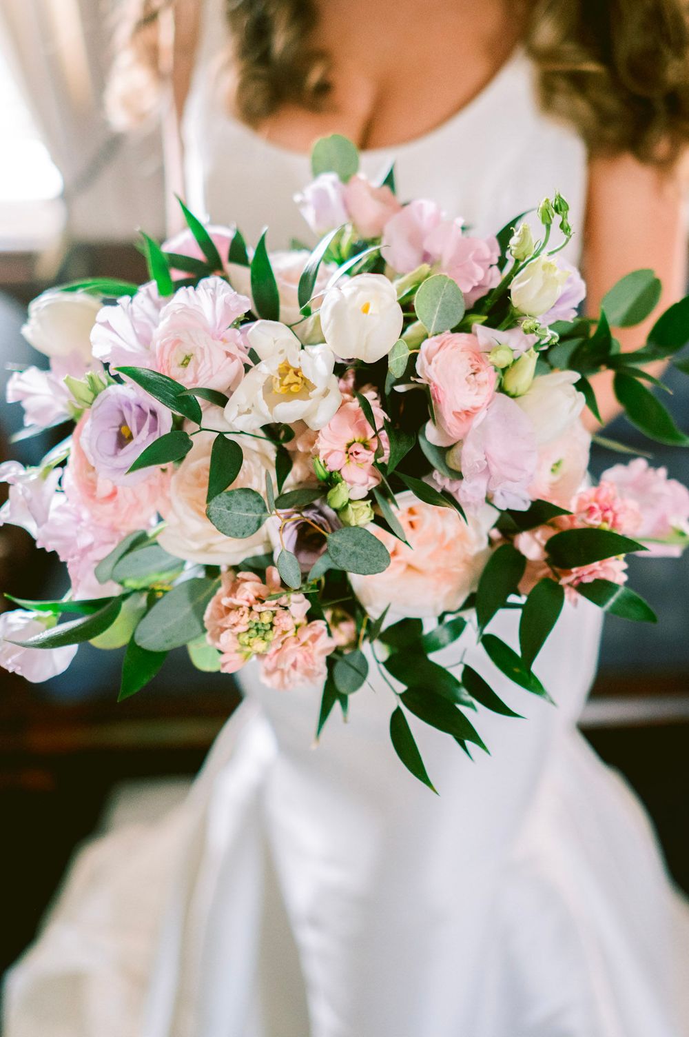 A delicate pink and white floral arrangement with carnations and greenery in a white vase creates an elegant display.