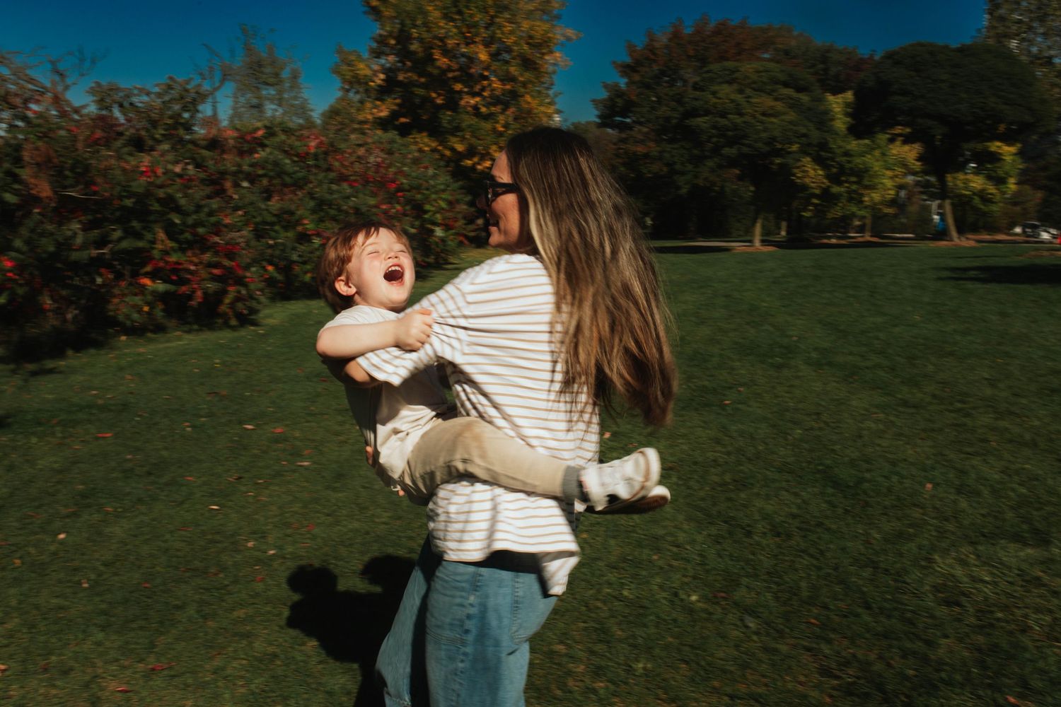 People enjoying a sunny autumn day in a park with golden trees and lush green grass.