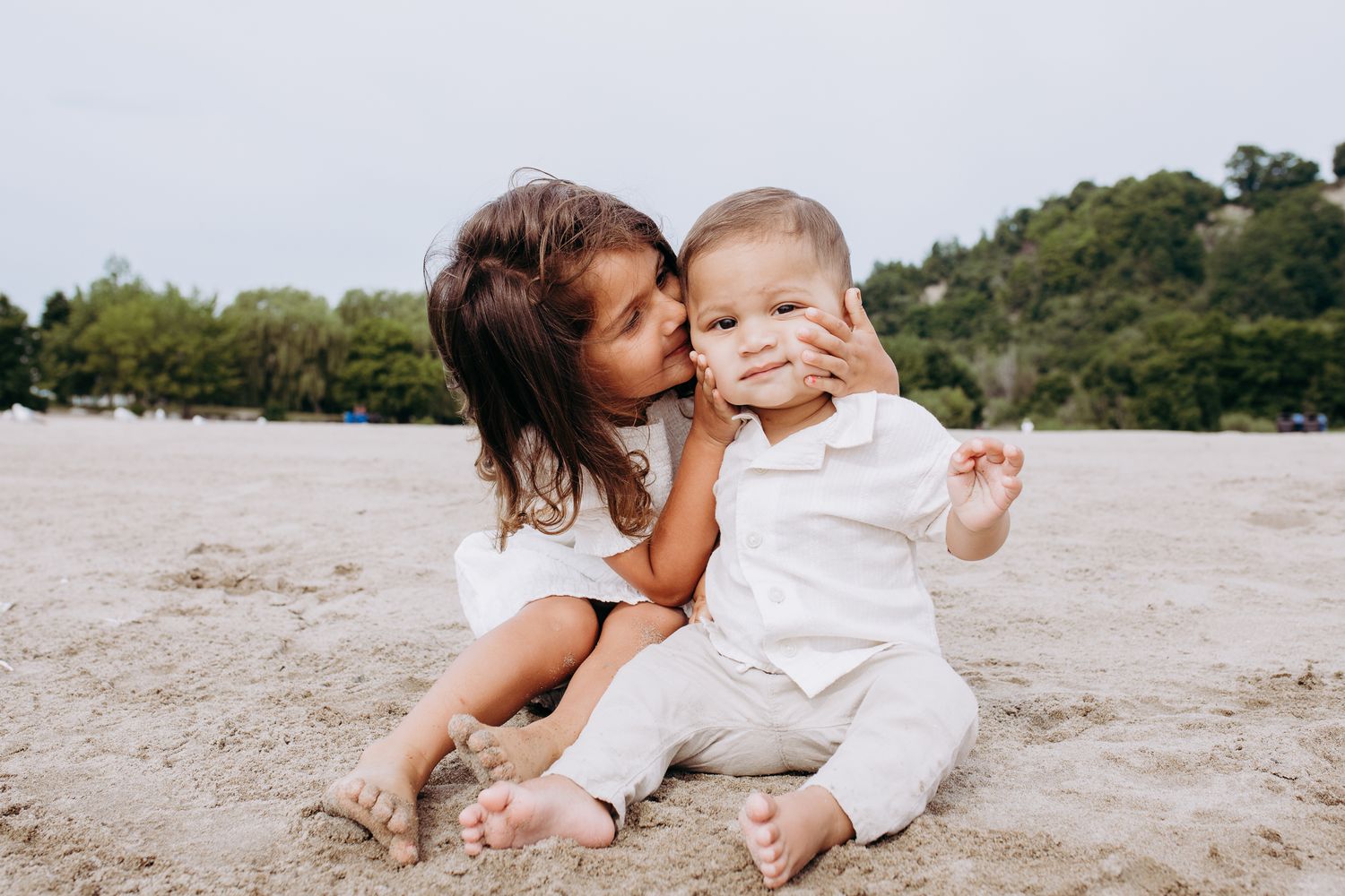 Heartwarming family moment captured on a sandy beach with green trees in the background.