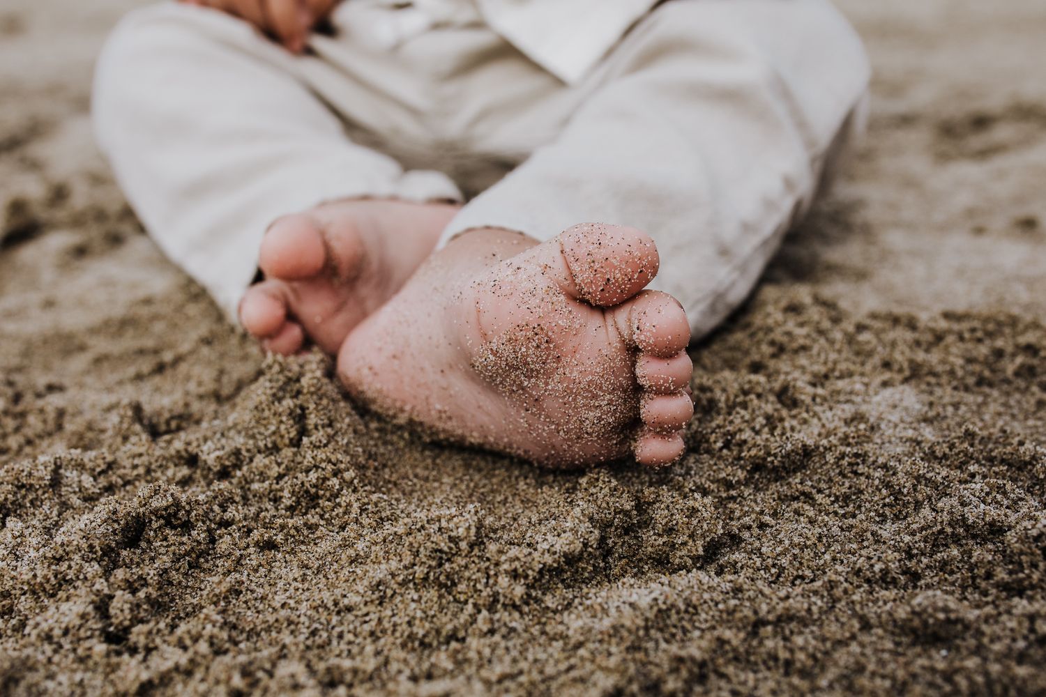 Close-up of sandy feet on beach with small grains of sand covering tiny toes.