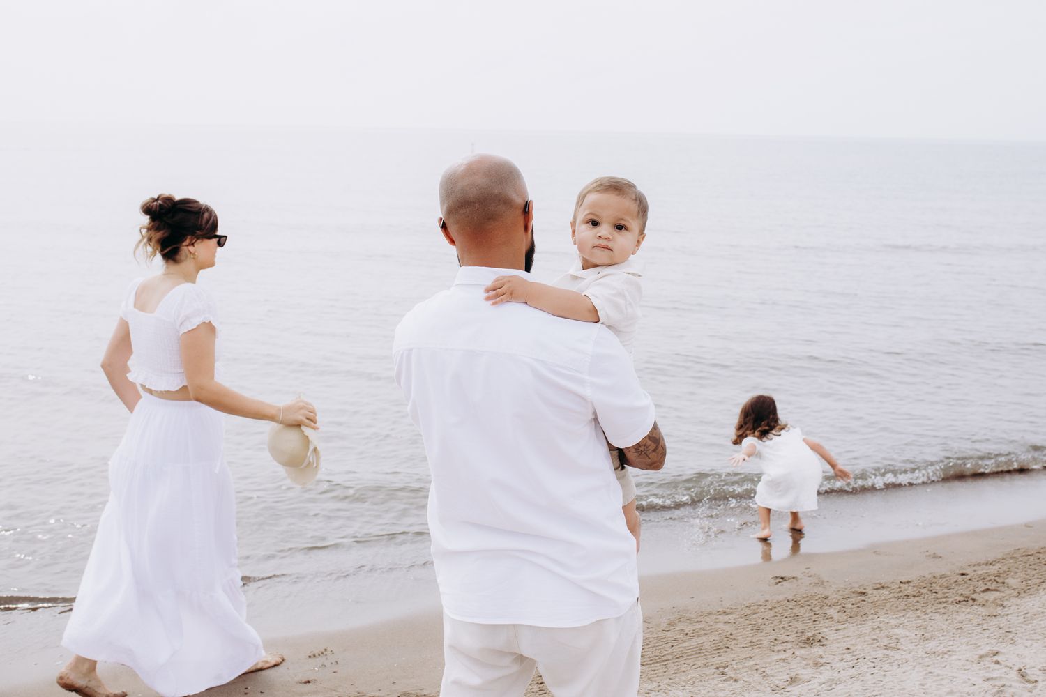 A family dressed in white outfits enjoys a peaceful moment together on a serene beach by the ocean.