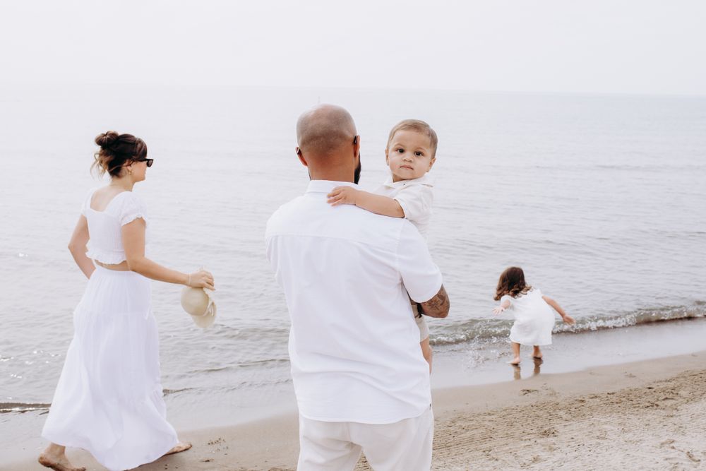 A family dressed in white outfits enjoys a peaceful moment together on a serene beach by the ocean.