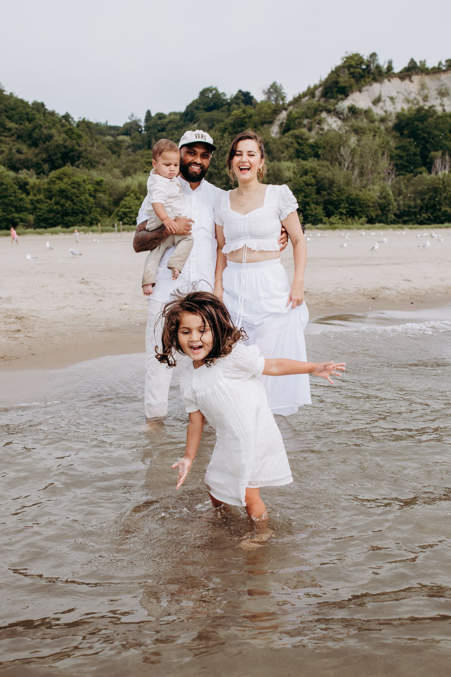 A cheerful family wearing white outfits plays together at the beach with cliff views in the background.