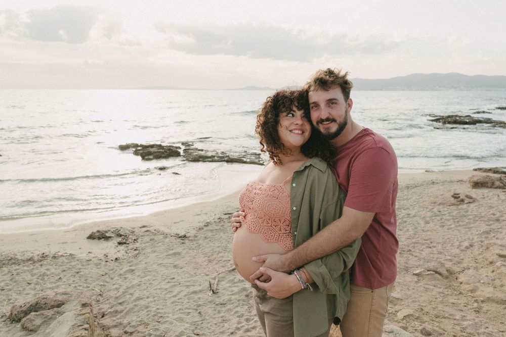 una pareja se abraza en la playa durante el atardecer esperando el nacimiento de su hijo