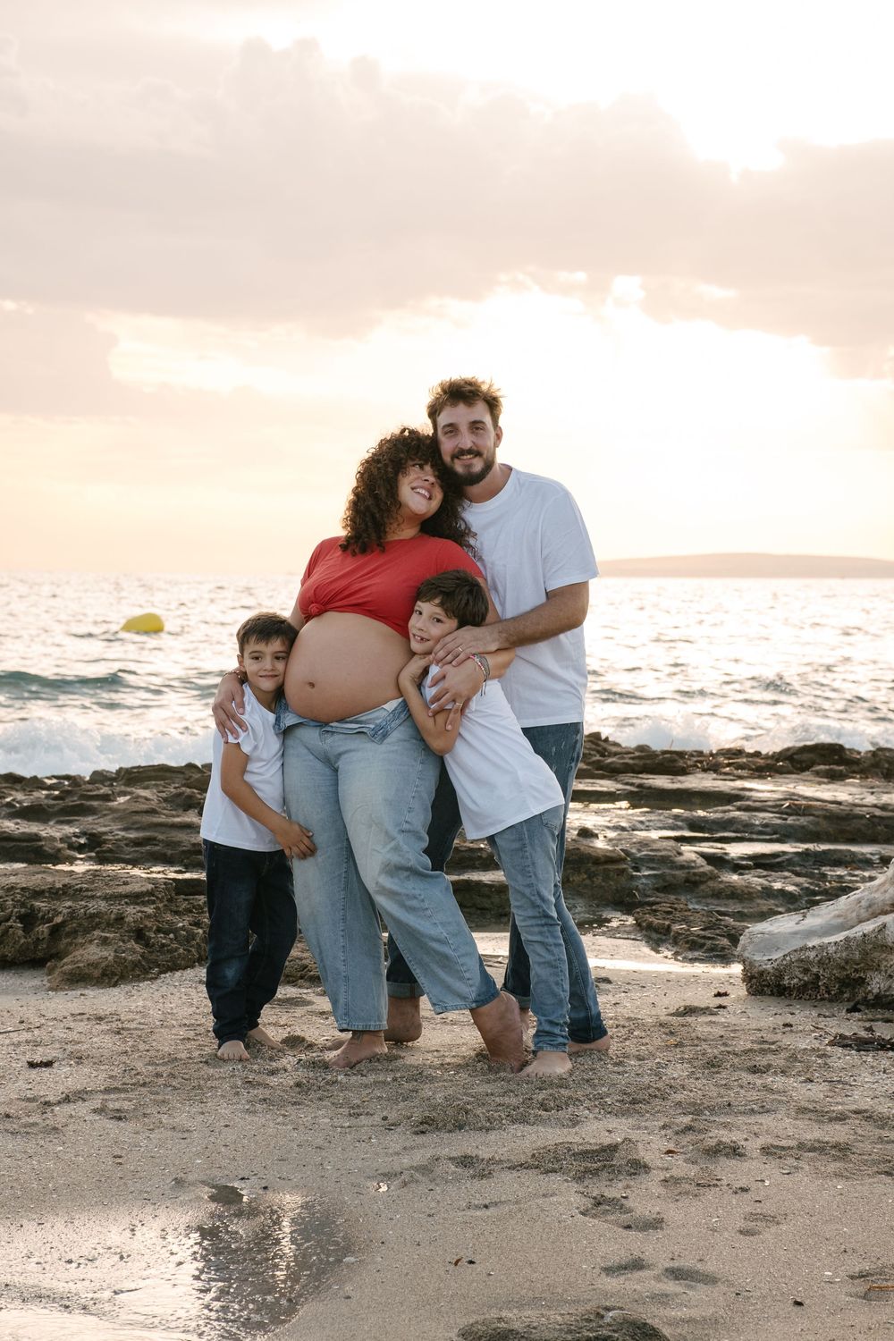 Family group embracing on a scenic beach with waves and sunset in the background.