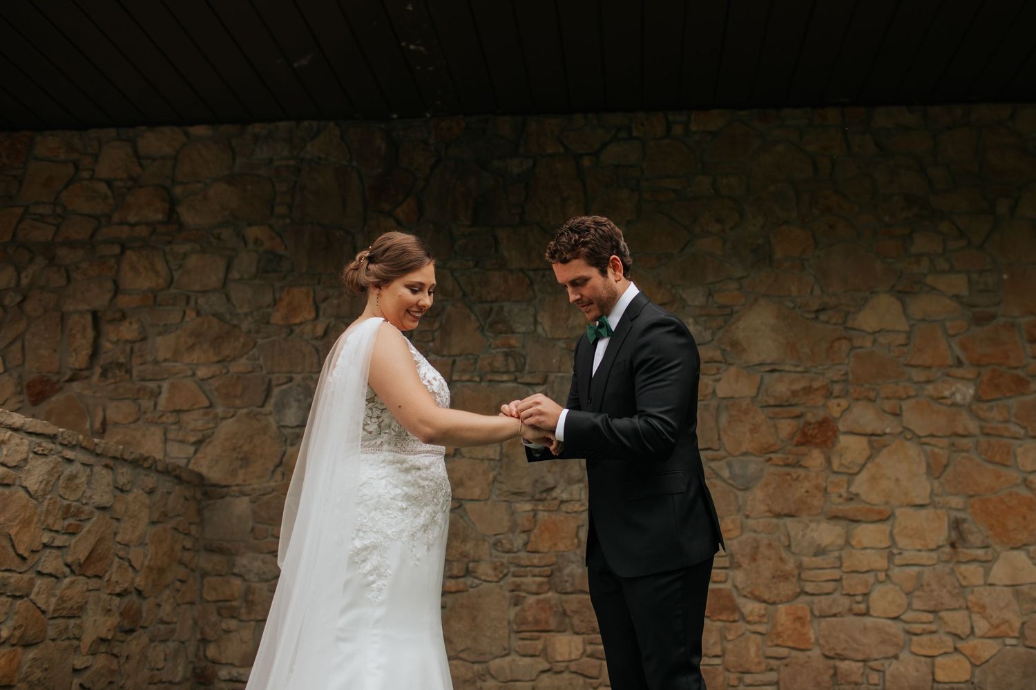 A couple shares an intimate dance moment during their wedding celebration against a rustic stone wall backdrop.