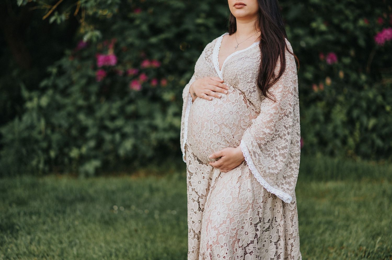 Delicate lace maternity dress photographed in a garden with blooming flowers.