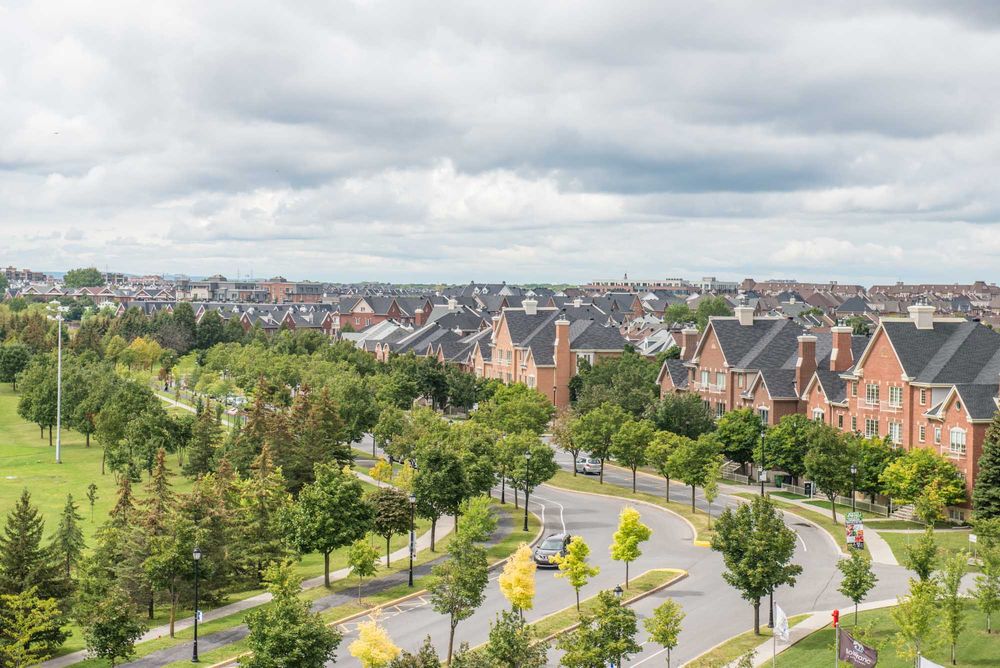 Aerial panorama of suburban neighborhood with rows of houses and green spaces under cloudy sky.