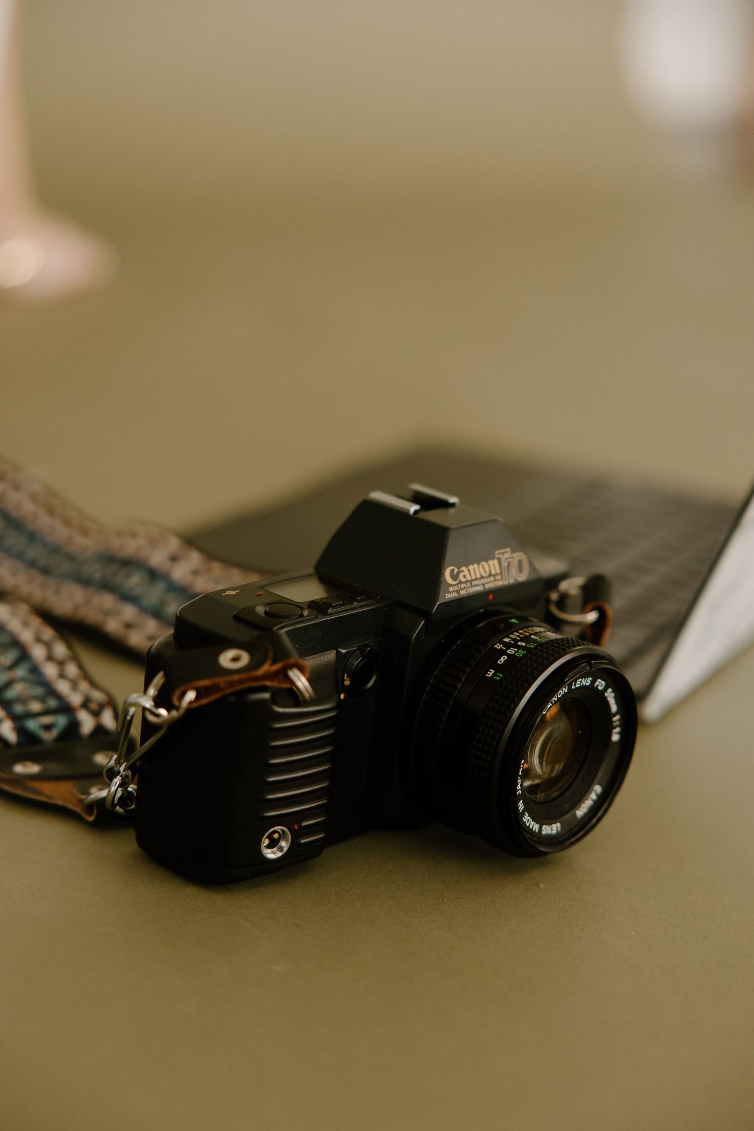 Vintage Canon film camera with a patterned strap resting on a surface in soft focus.