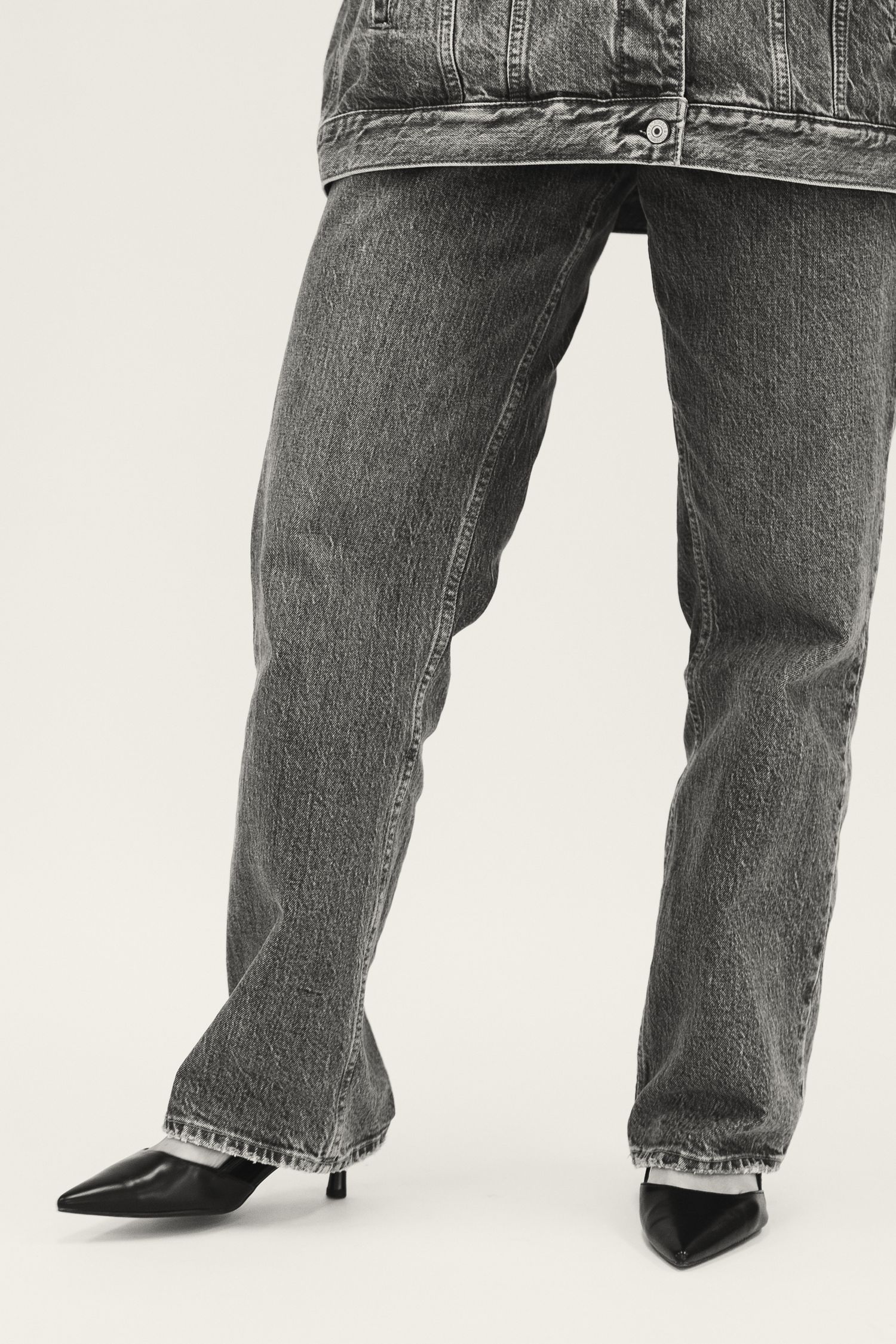Close-up of gray wash wide-leg jeans with black kitten heel shoes on white background.