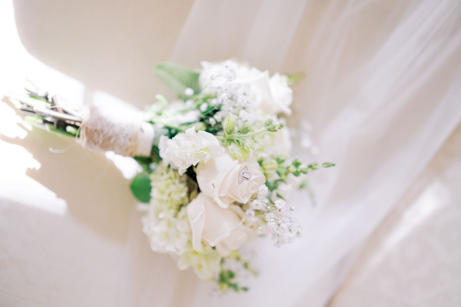 White floral bouquets with delicate greenery arranged on a light fabric background for a wedding celebration.
