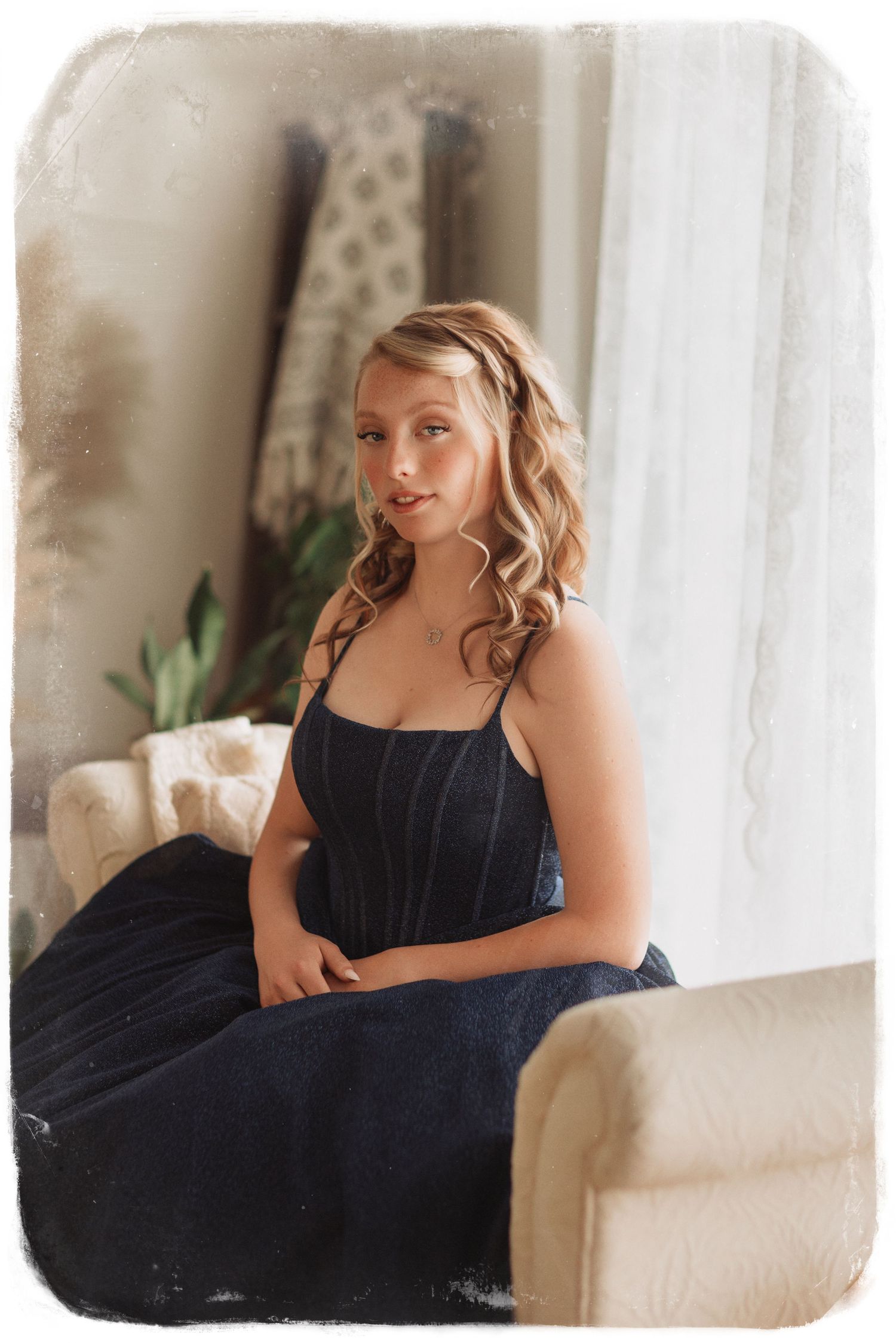 A figure in a navy blue dress poses elegantly on a white couch in a bright, sunlit room with minimalist decor.