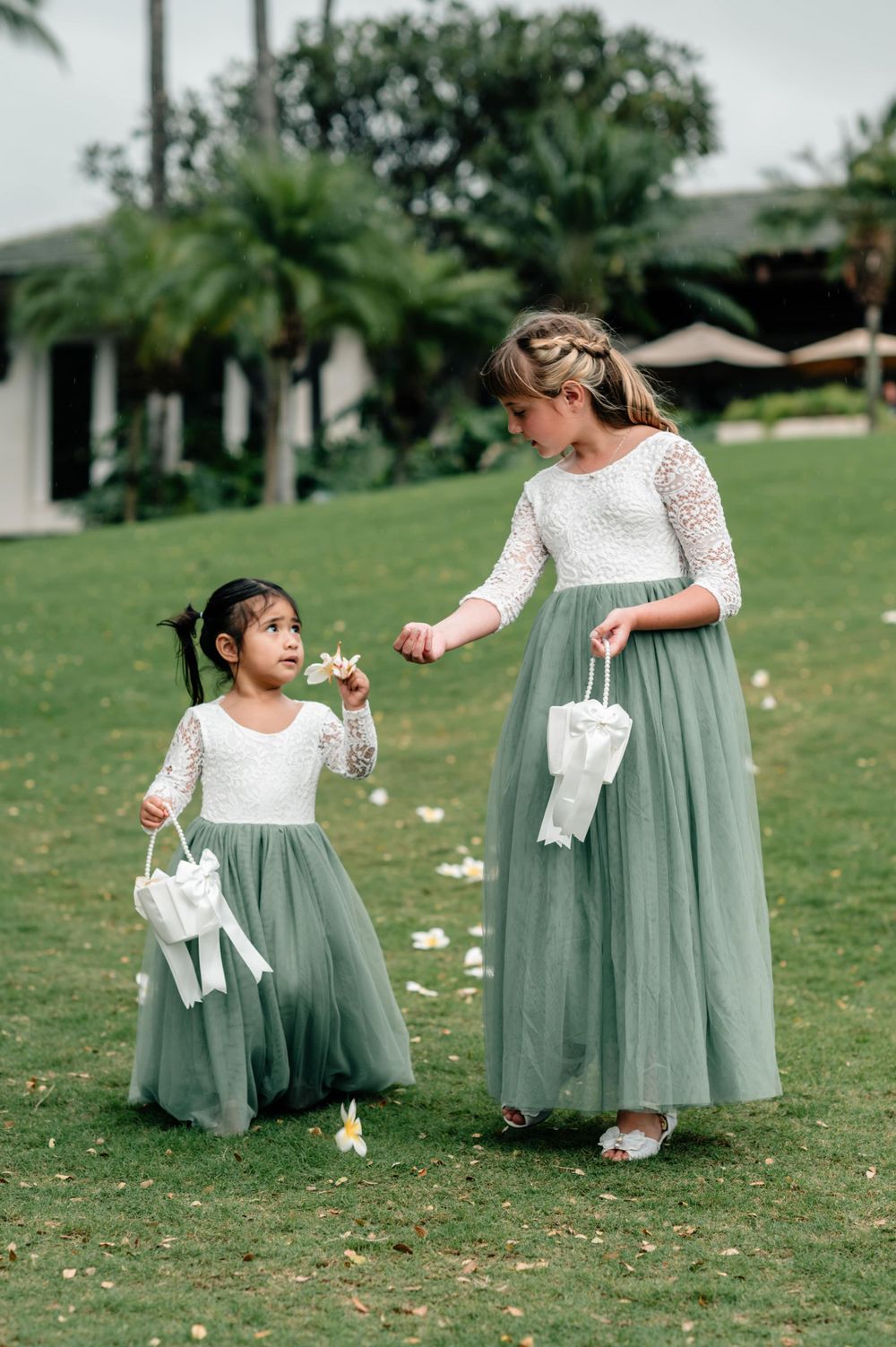 Children in sage green tulle dresses playing on grassy lawn at wedding.