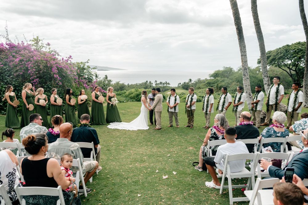 Outdoor wedding ceremony setup with white chairs and tropical landscape backdrop.