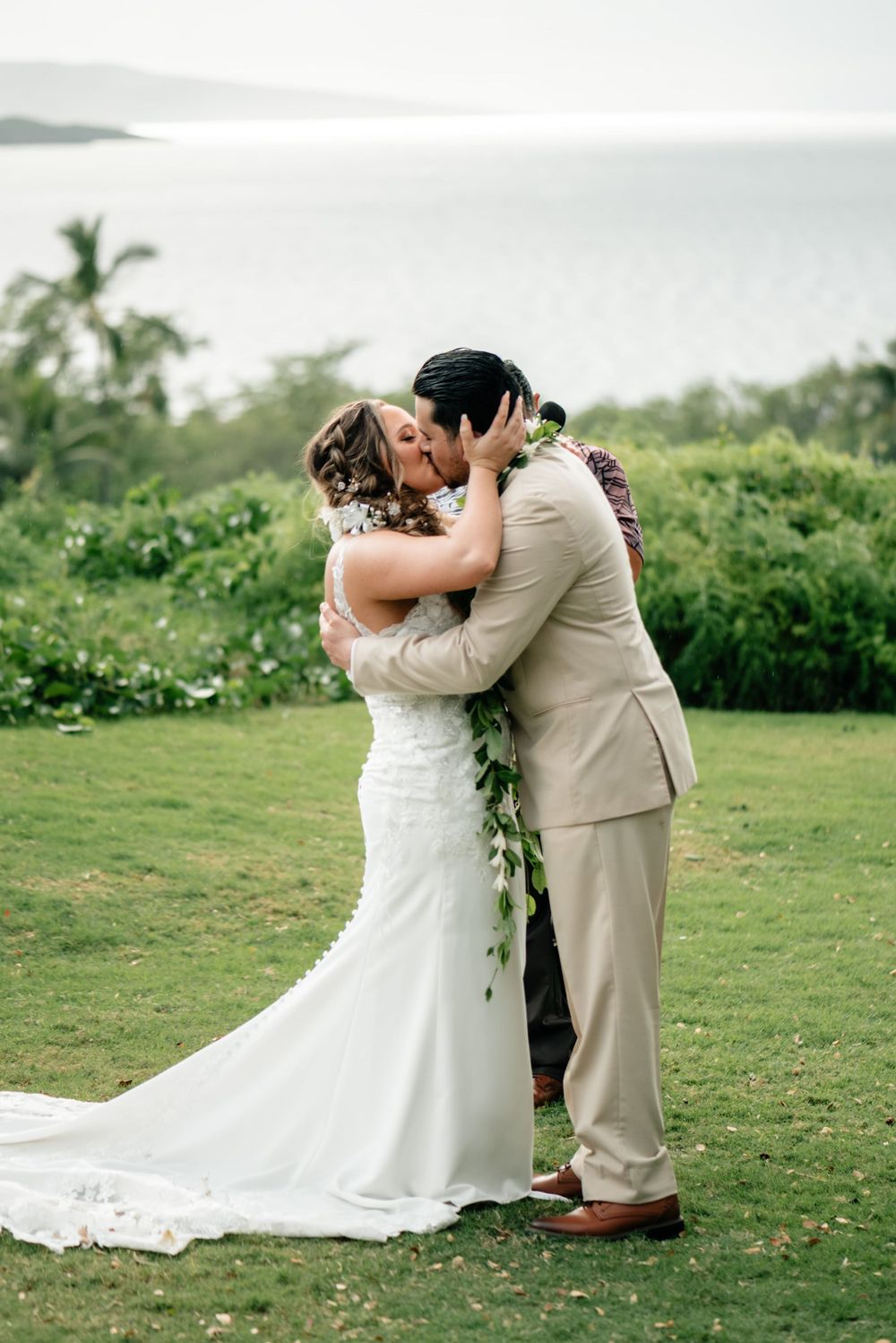 Romantic wedding couple sharing intimate moment on hilltop overlooking tropical landscape.