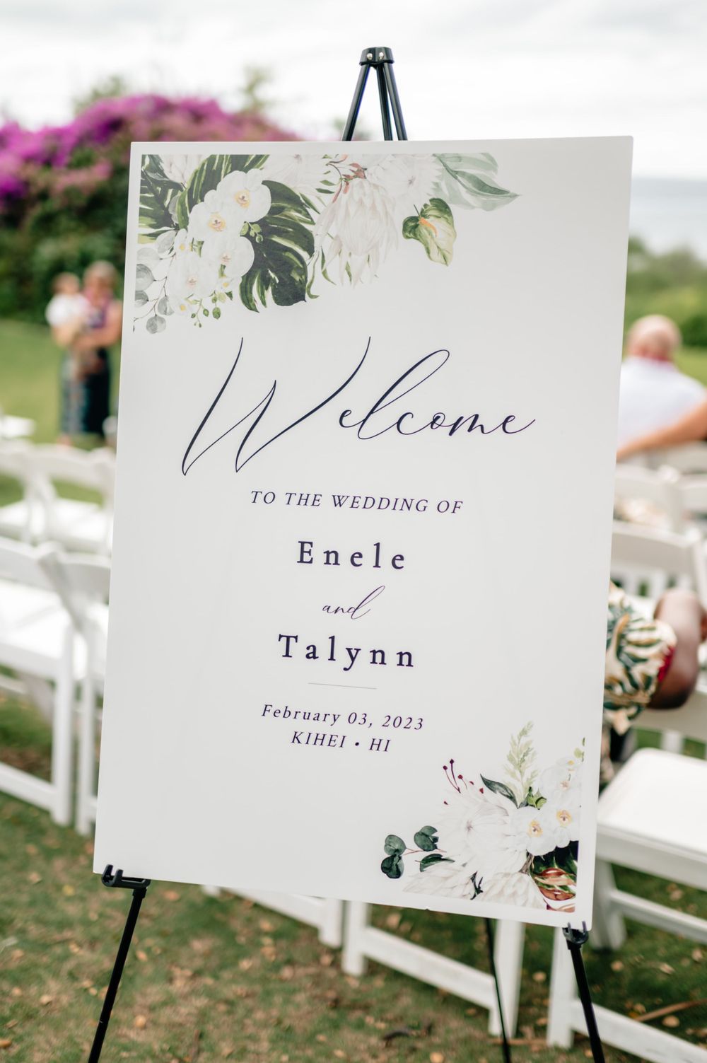 Elegant white wedding welcome signs with floral designs displayed on easels at outdoor ceremony.