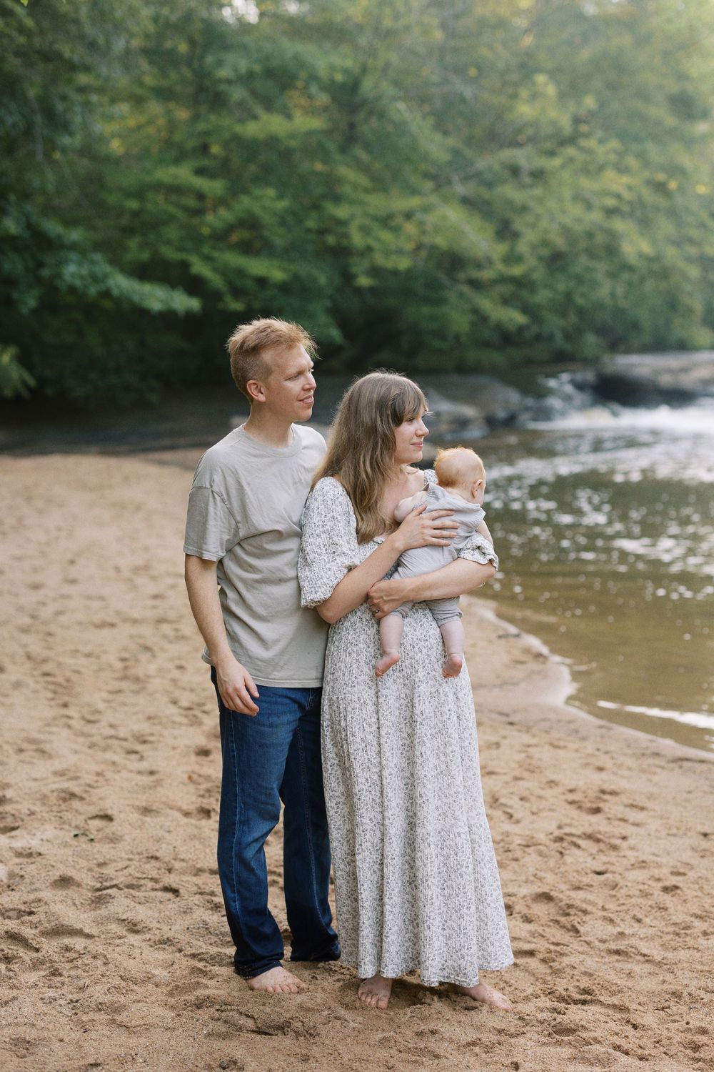 A group gathers on a peaceful riverbank with trees and flowing water in the background.