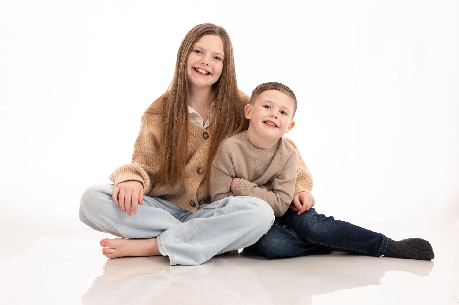 A family lying together on a white background in a studio setting, wearing casual clothing and smiling.