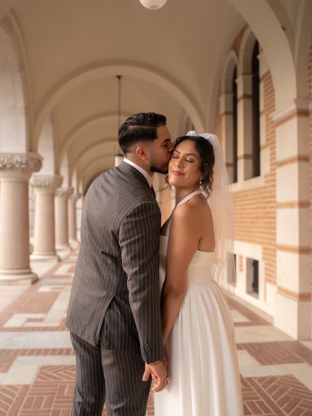 Rubi and Joe walking hand in hand on the paths of Rice University for their wedding portrait session, with sunlight filtering through trees