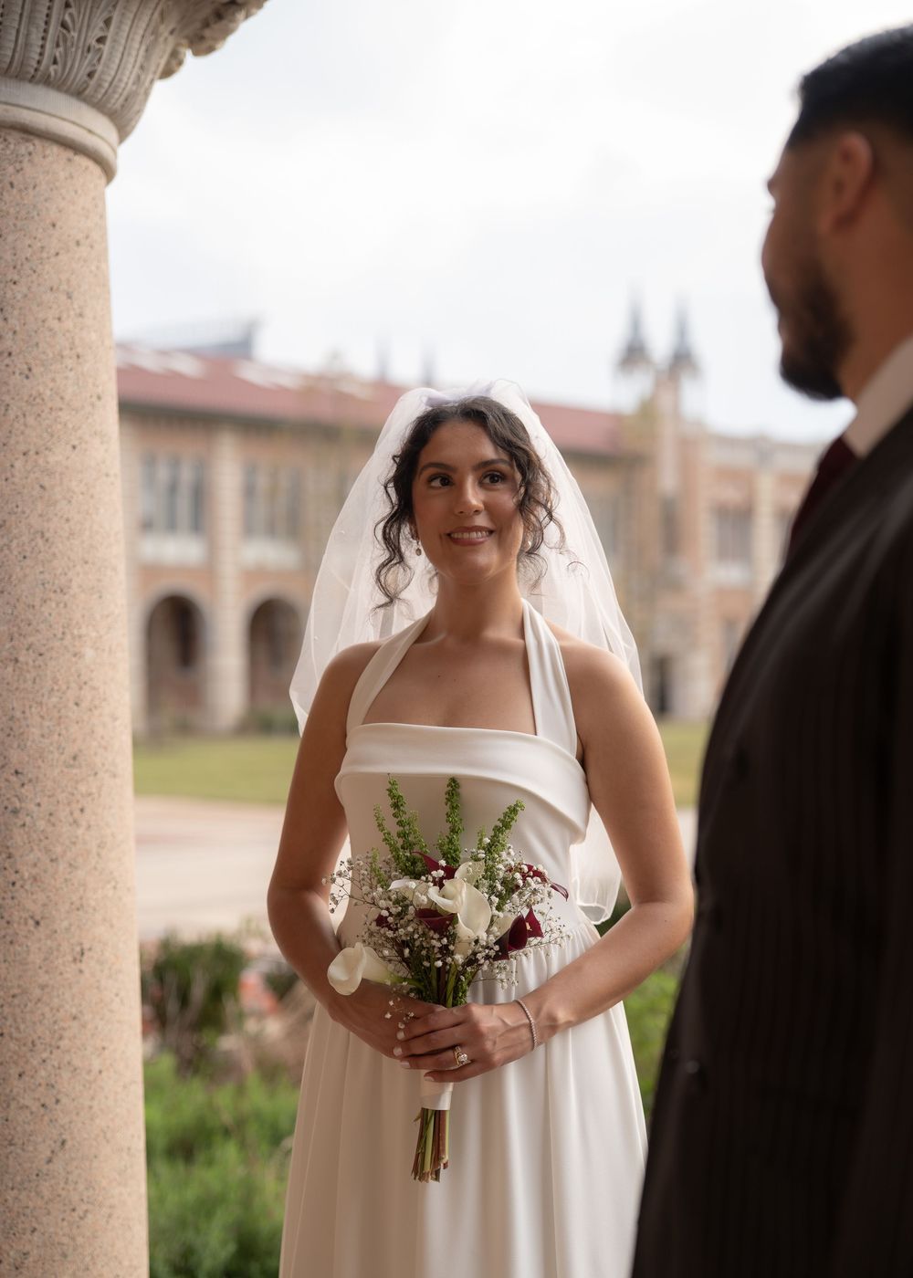 Rubi and Joe walking hand in hand on the paths of Rice University for their wedding portrait session, with sunlight filtering through trees