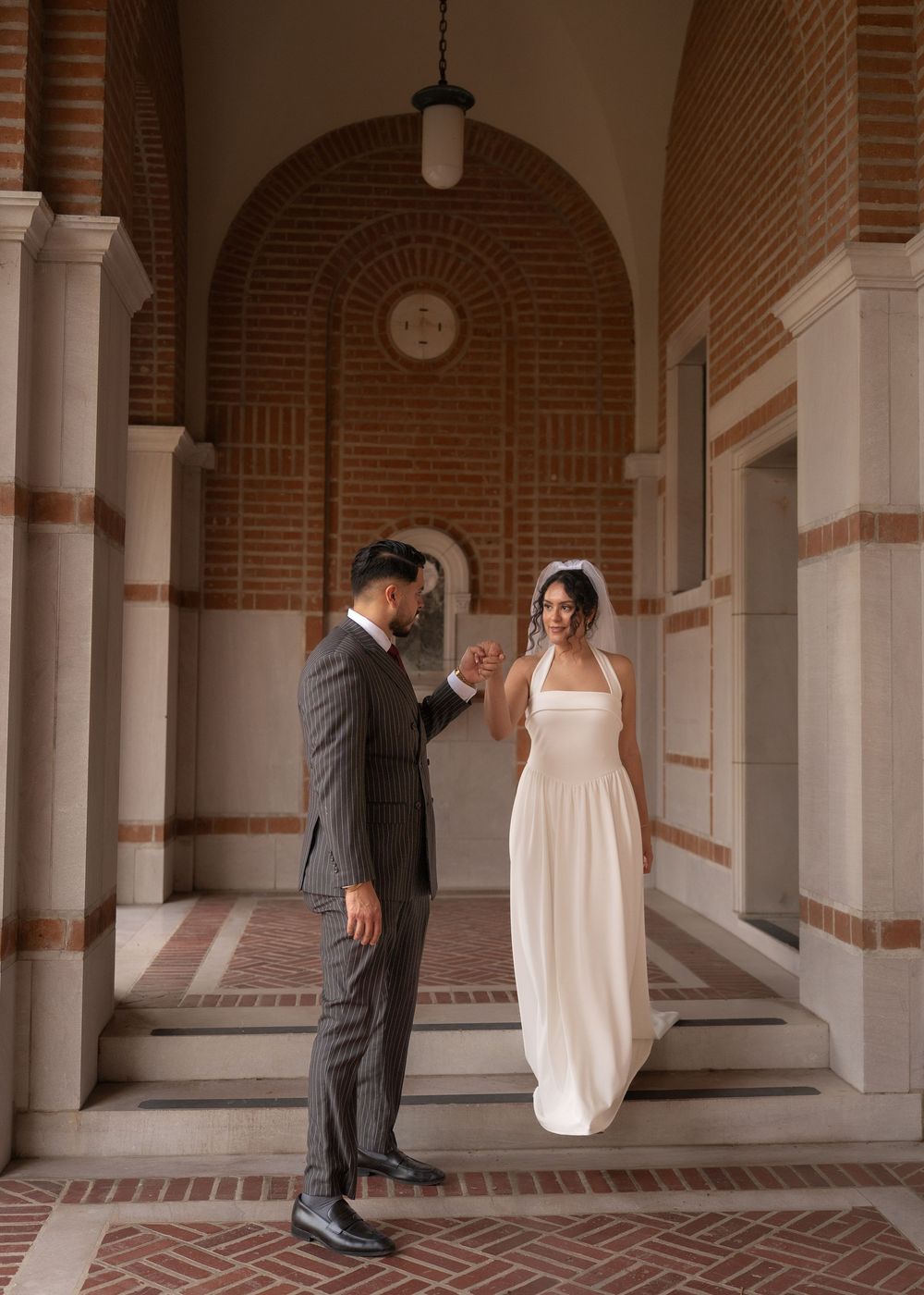 Rubi and Joe walking hand in hand on the paths of Rice University for their wedding portrait session, with sunlight filtering through trees