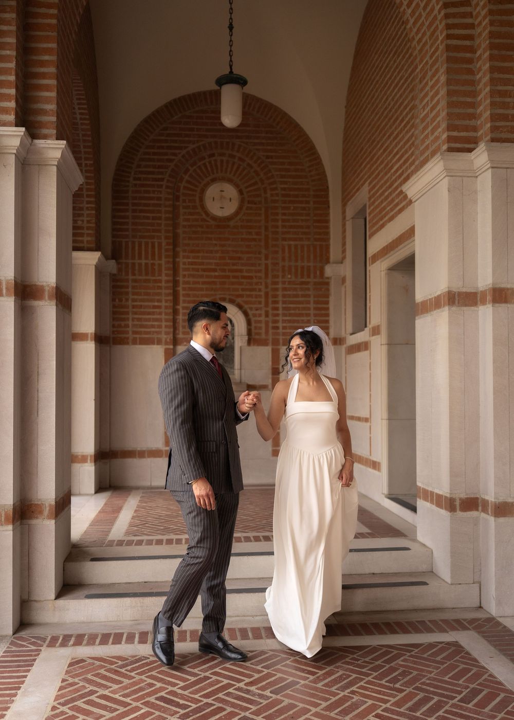 Rubi and Joe walking hand in hand on the paths of Rice University for their wedding portrait session, with sunlight filtering through trees