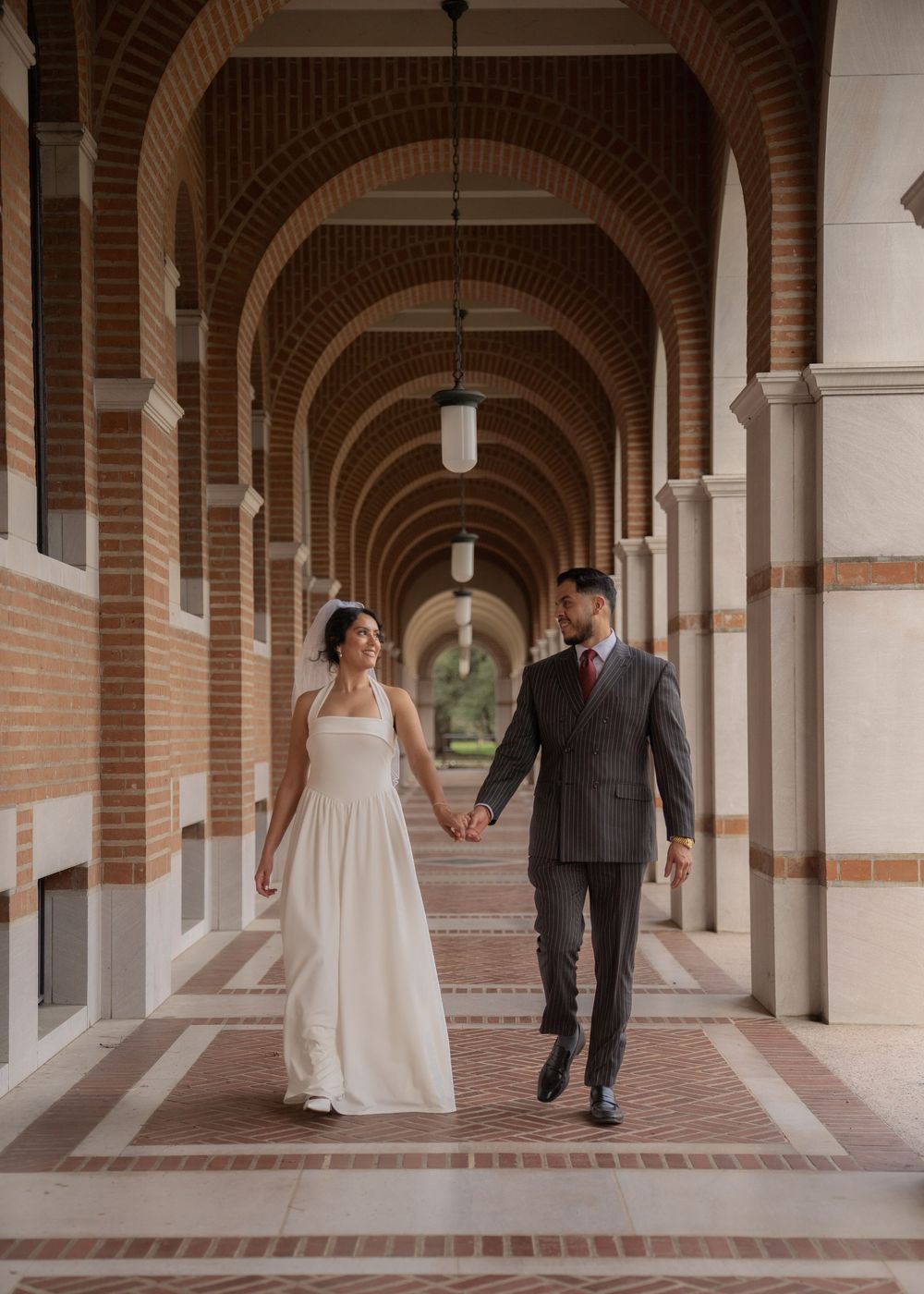 Rubi and Joe walking hand in hand on the paths of Rice University for their wedding portrait session, with sunlight filtering through trees