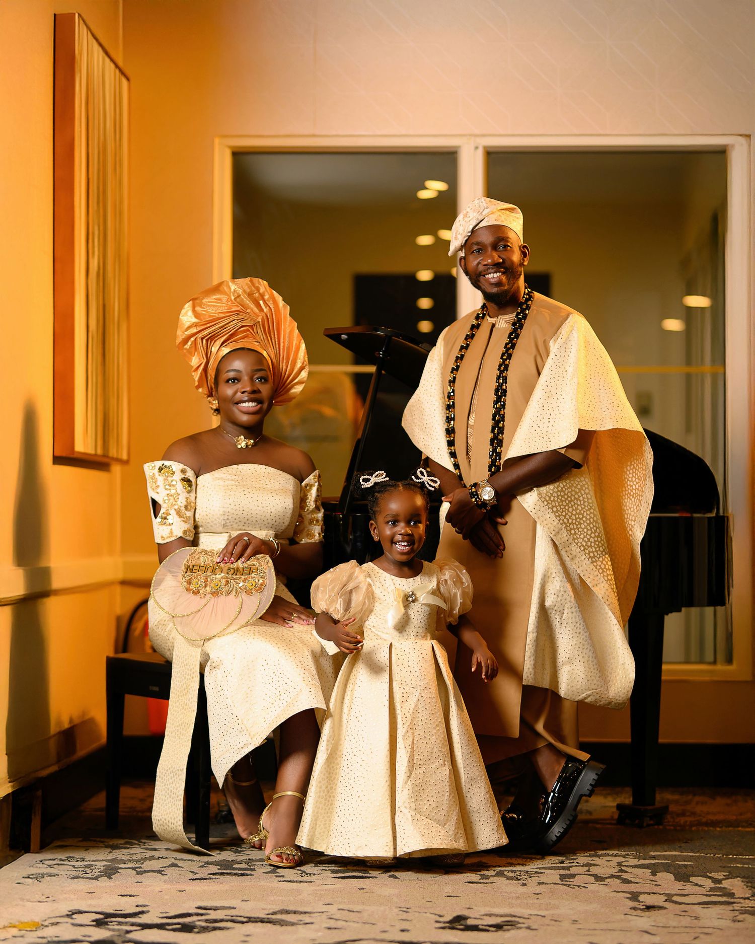 People in traditional white African attire sit and pose together in a warm-lit hallway setting.