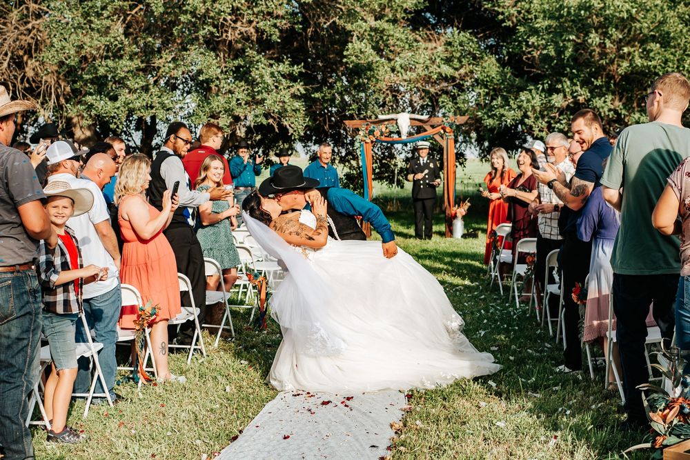 Wedding celebration in an outdoor garden setting with guests lining a white aisle runner during a sunny ceremony.
