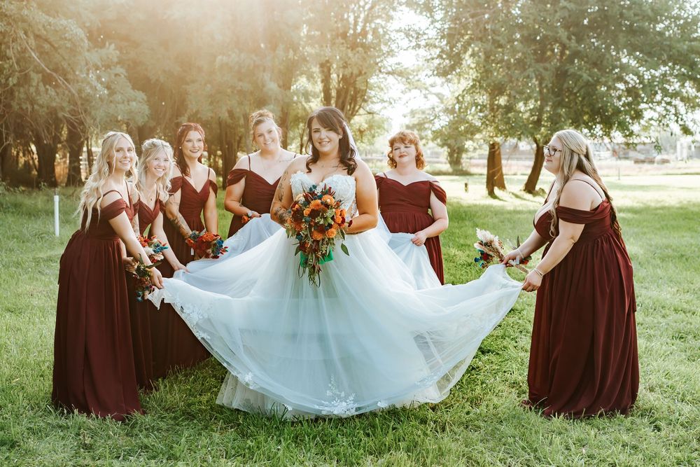 Wedding party in burgundy dresses and white gown pose together in a scenic outdoor setting during autumn.