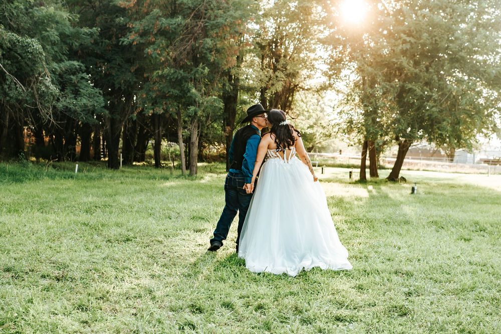 A couple in wedding attire walks together through a sunlit park during golden hour.