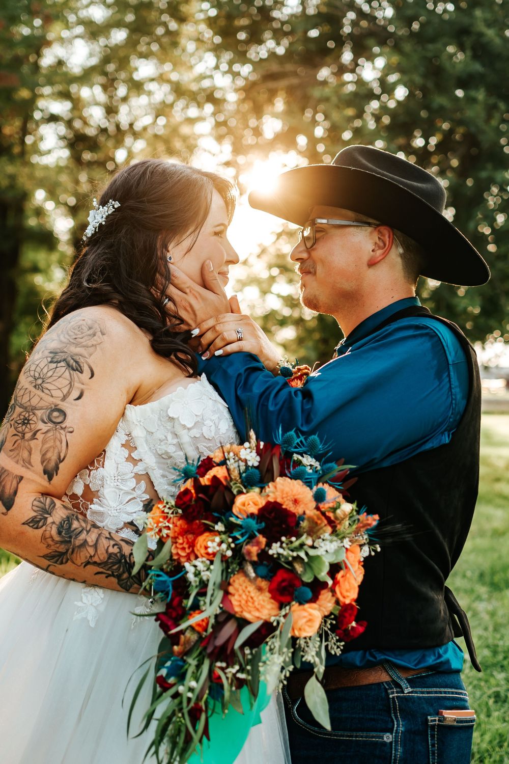 A romantic sunset wedding photo showing a couple embracing outdoors with a vibrant orange and blue bouquet.
