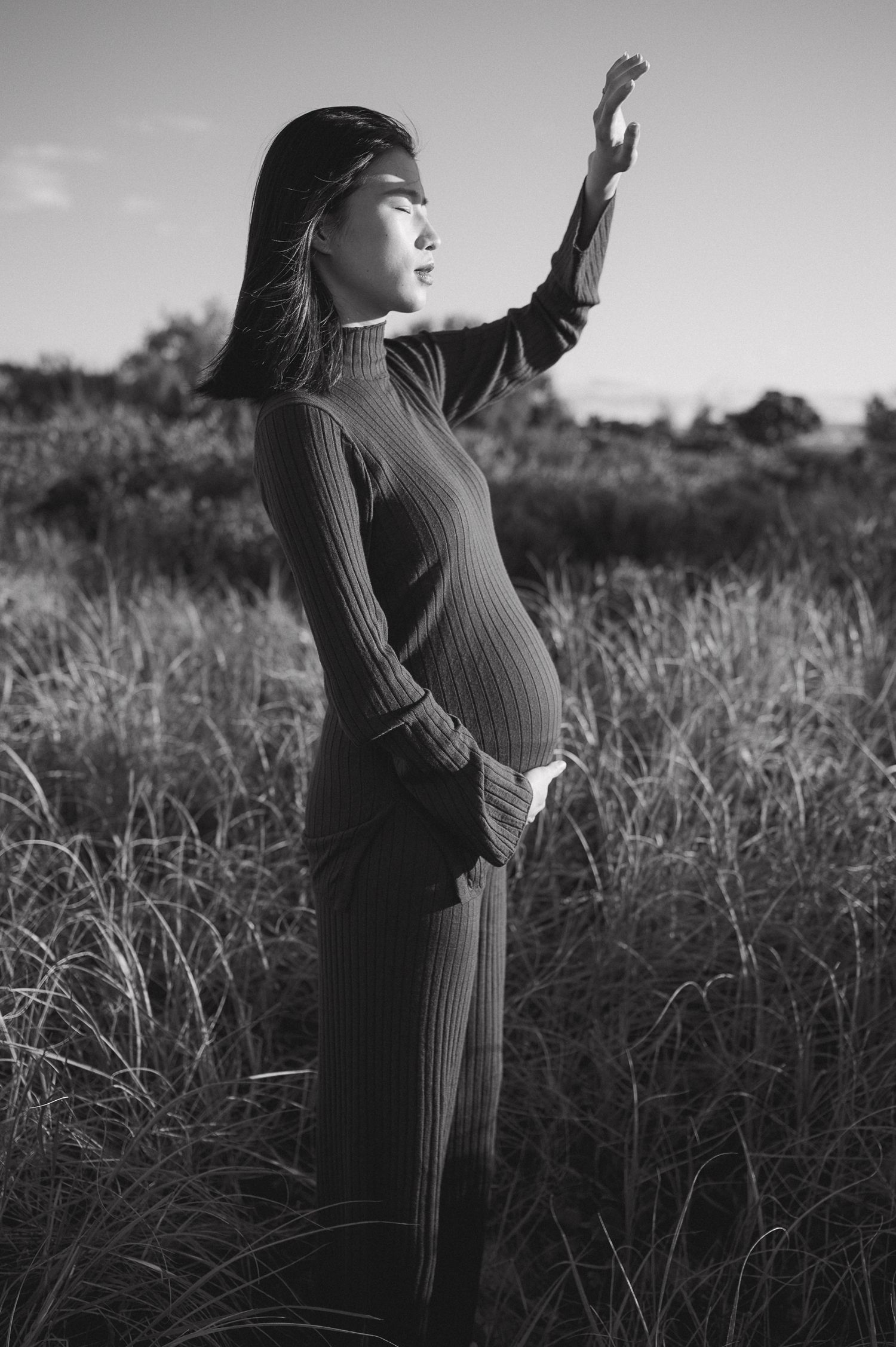 Black and white photos of woman in ribbed dress posing expressively in field.