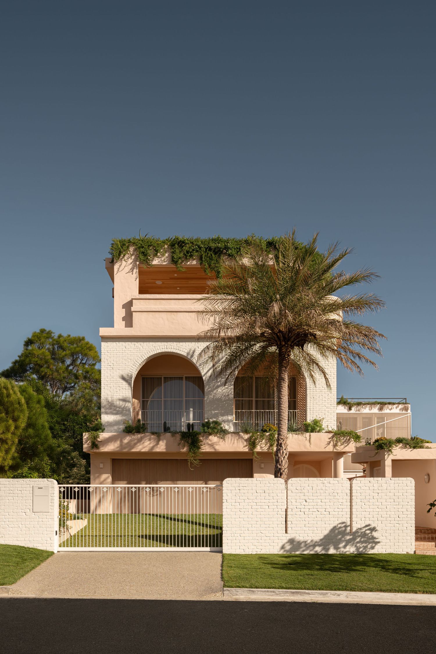 Mediterranean style luxury home with palm tree and white perimeter wall features arched windows and rooftop garden.