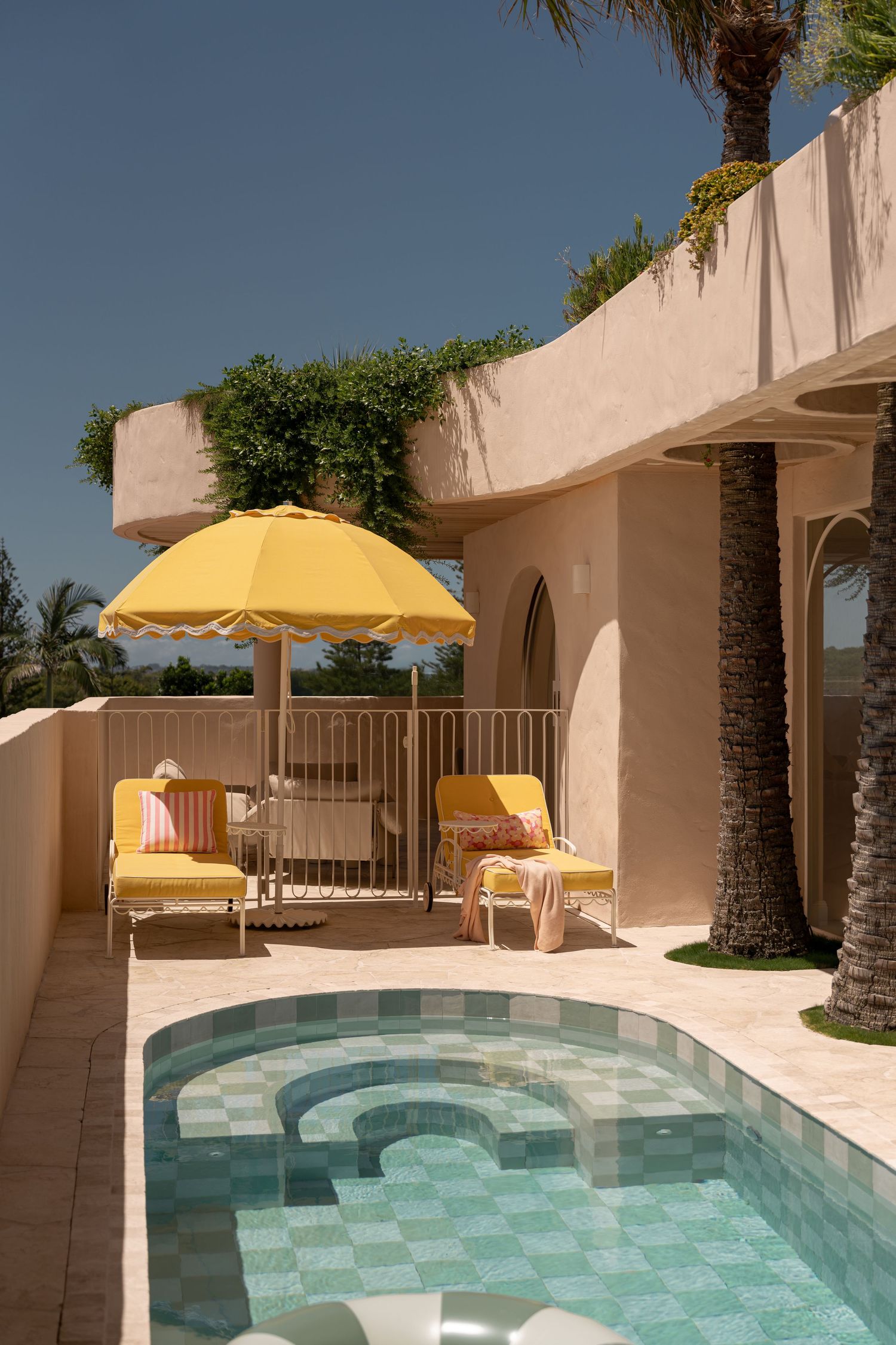 Curved swimming pool with turquoise water surrounded by beige walls and yellow umbrellas at a modern resort property.