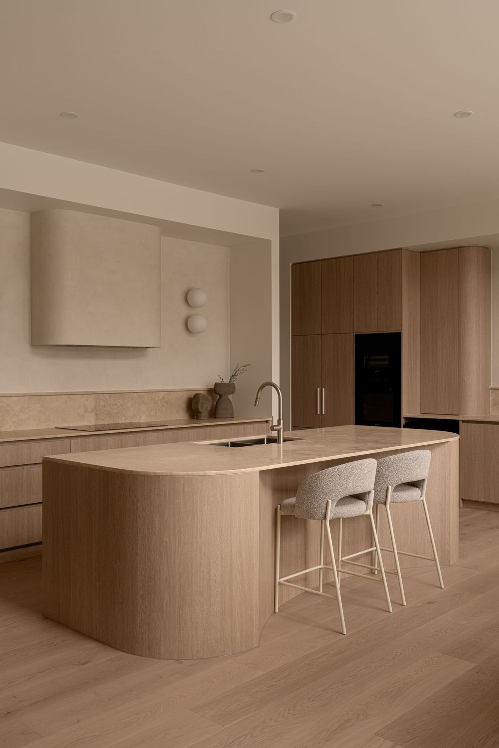 Modern minimalist kitchen with light wood cabinetry, white countertops, and bar seating in a monochromatic neutral palette.