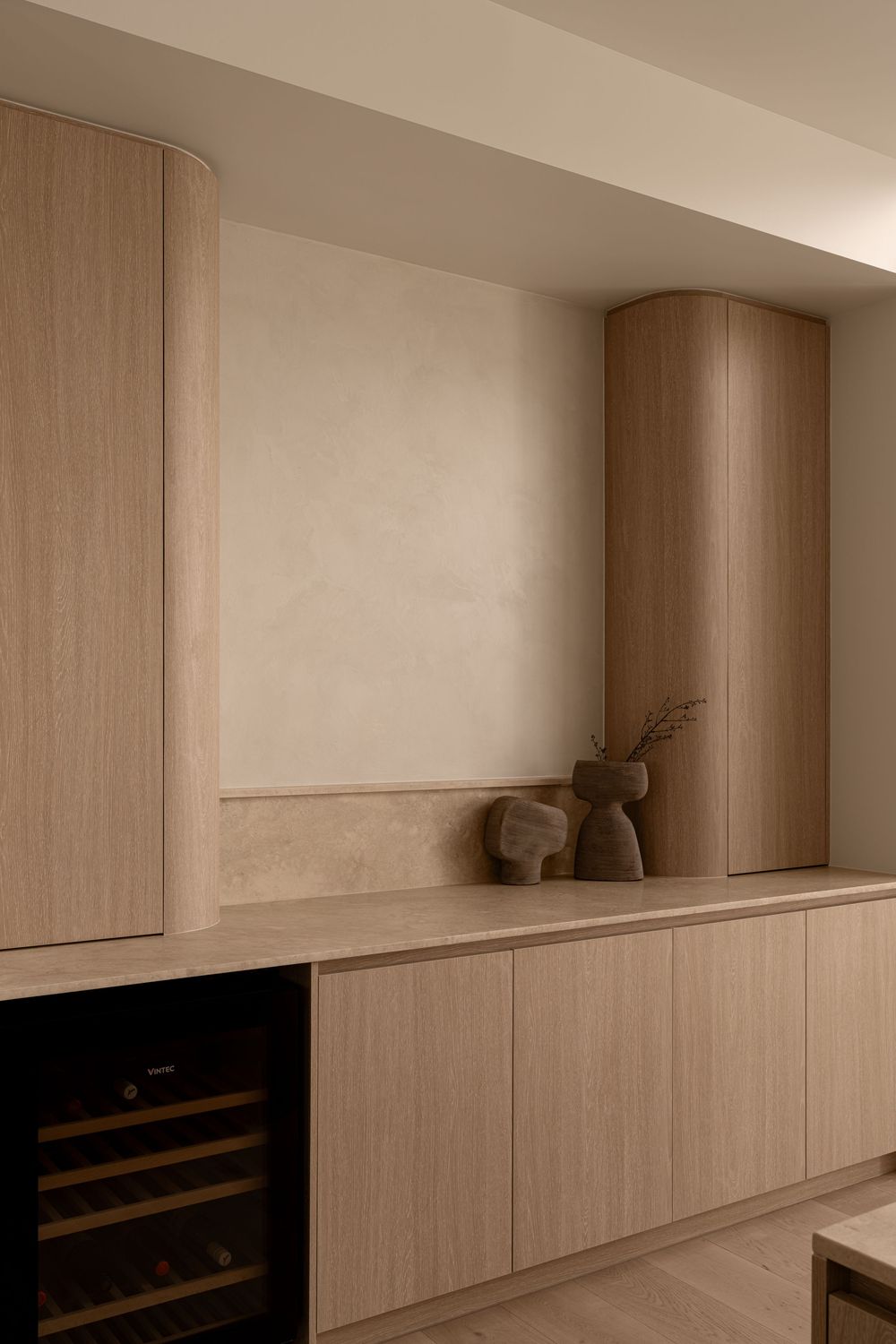 Modern built-in cabinetry with wine fridge and light wood finish features minimalist design and decorative vase display.