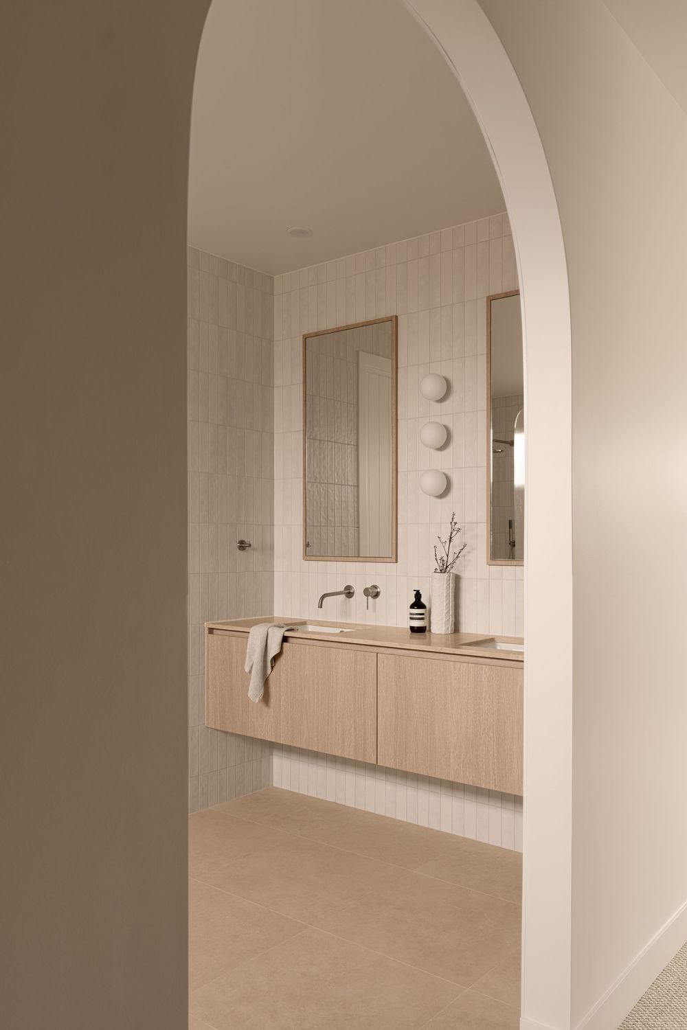 Modern minimalist bathroom interior with curved archway, light wood vanity, and neutral beige tones throughout.