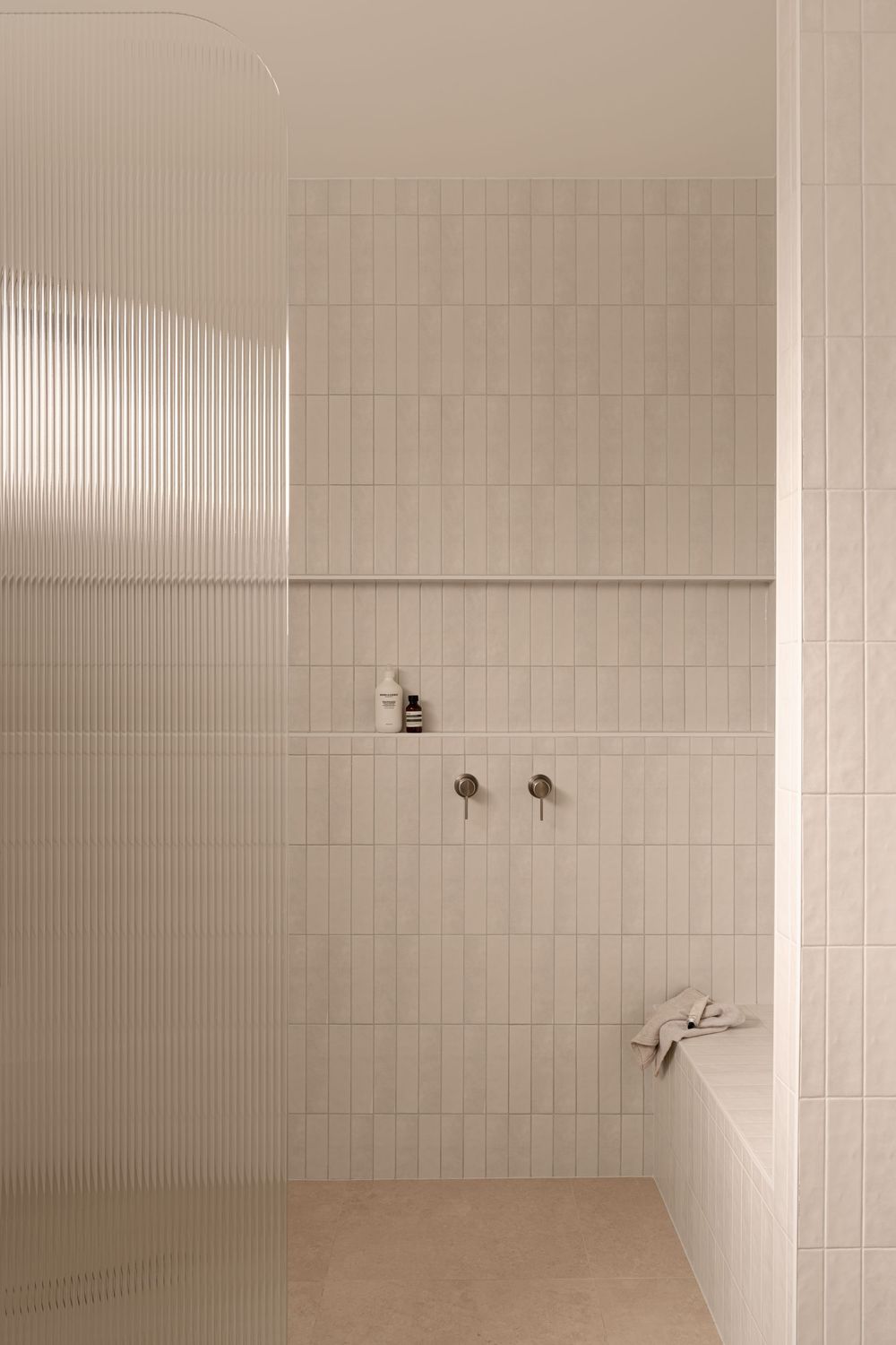 Minimalist white tiled bathroom interior with empty walls and simple plumbing fixtures in a modern design aesthetic.