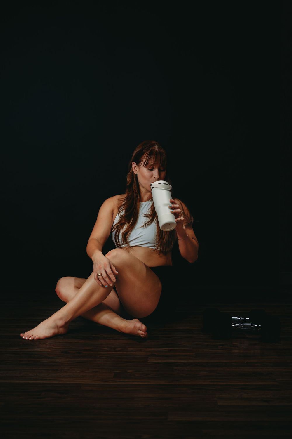 Person in athletic wear resting on dark wooden floor with water bottle.