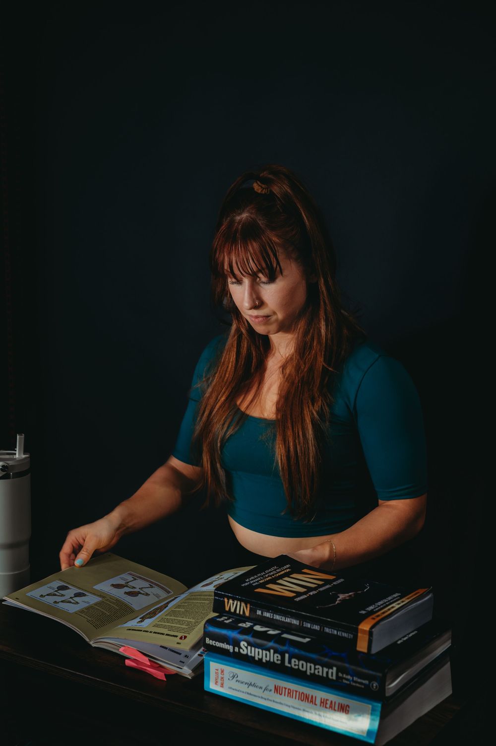 Person in teal shirt reading books in moody dark setting with dramatic lighting.