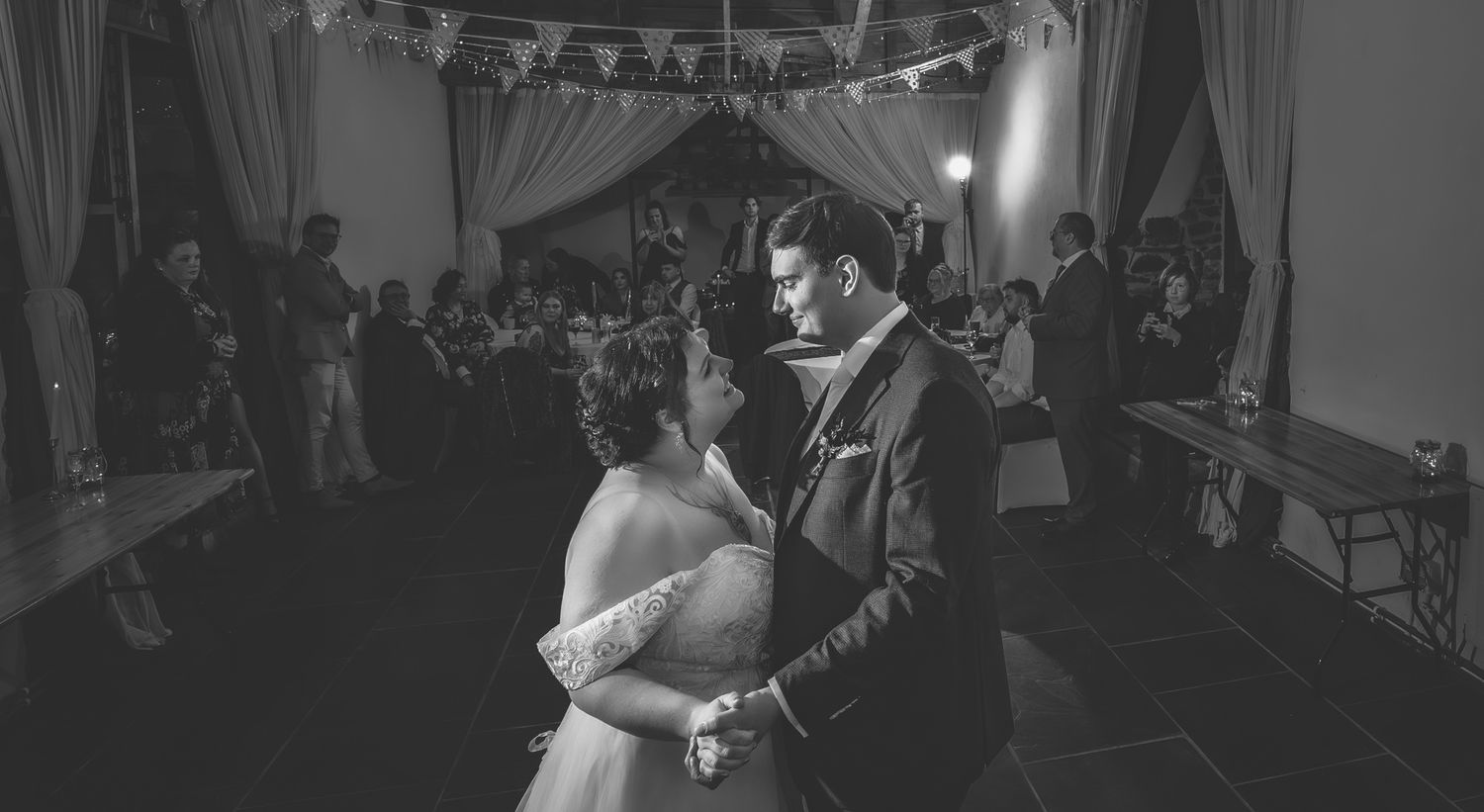 Couples dance together at a dimly lit wedding reception with string lights overhead.